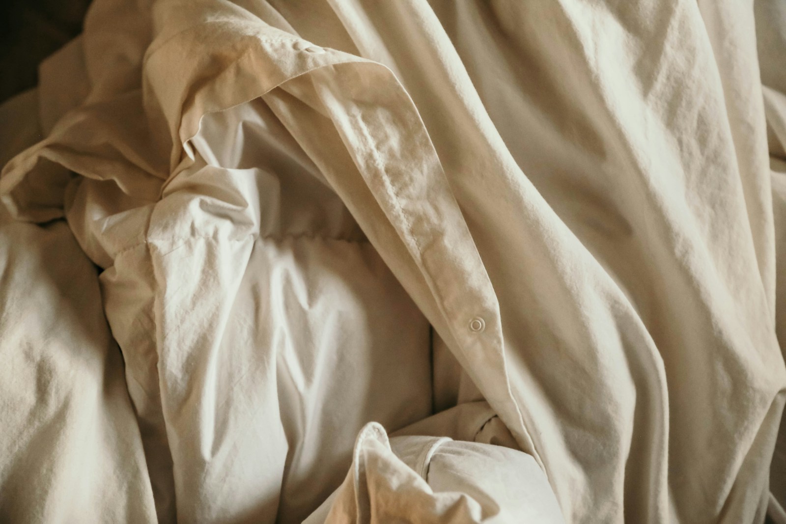 an unmade bed with white sheets and pillows